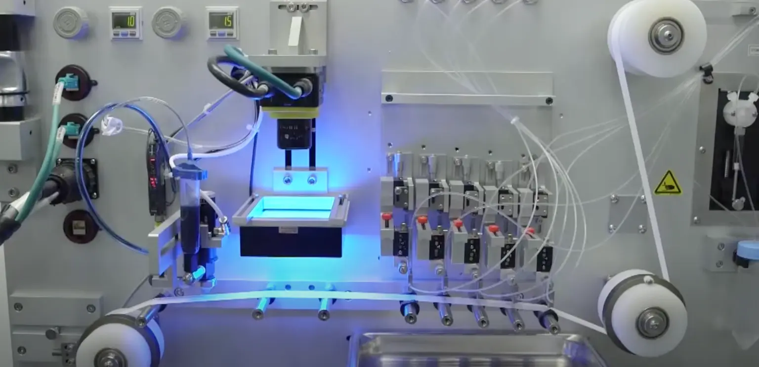 Close-up of a laboratory automation machine with tubes, control switches, and a blue light illuminating a central component.